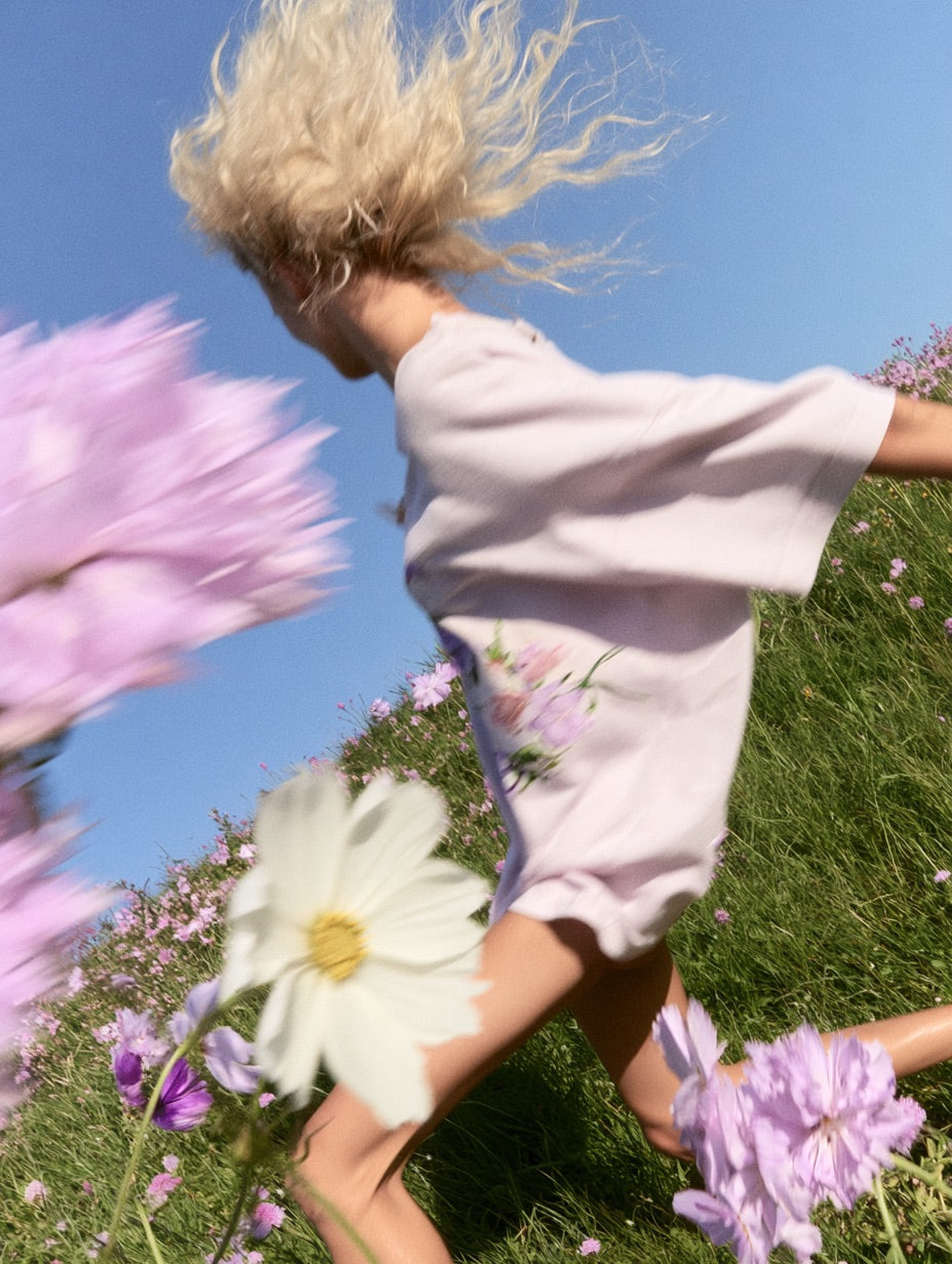 Running through a meadow of pink cosmos flowers in a lavender tee